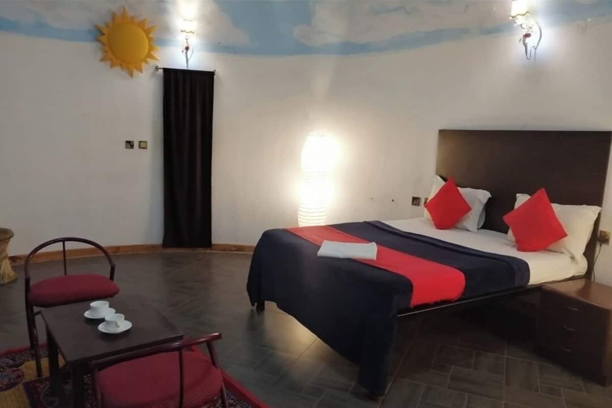 Une chambre d’hôtel avec un lit, une table et des chaises, une décoration représentant un soleil au mur et une table de chevet.