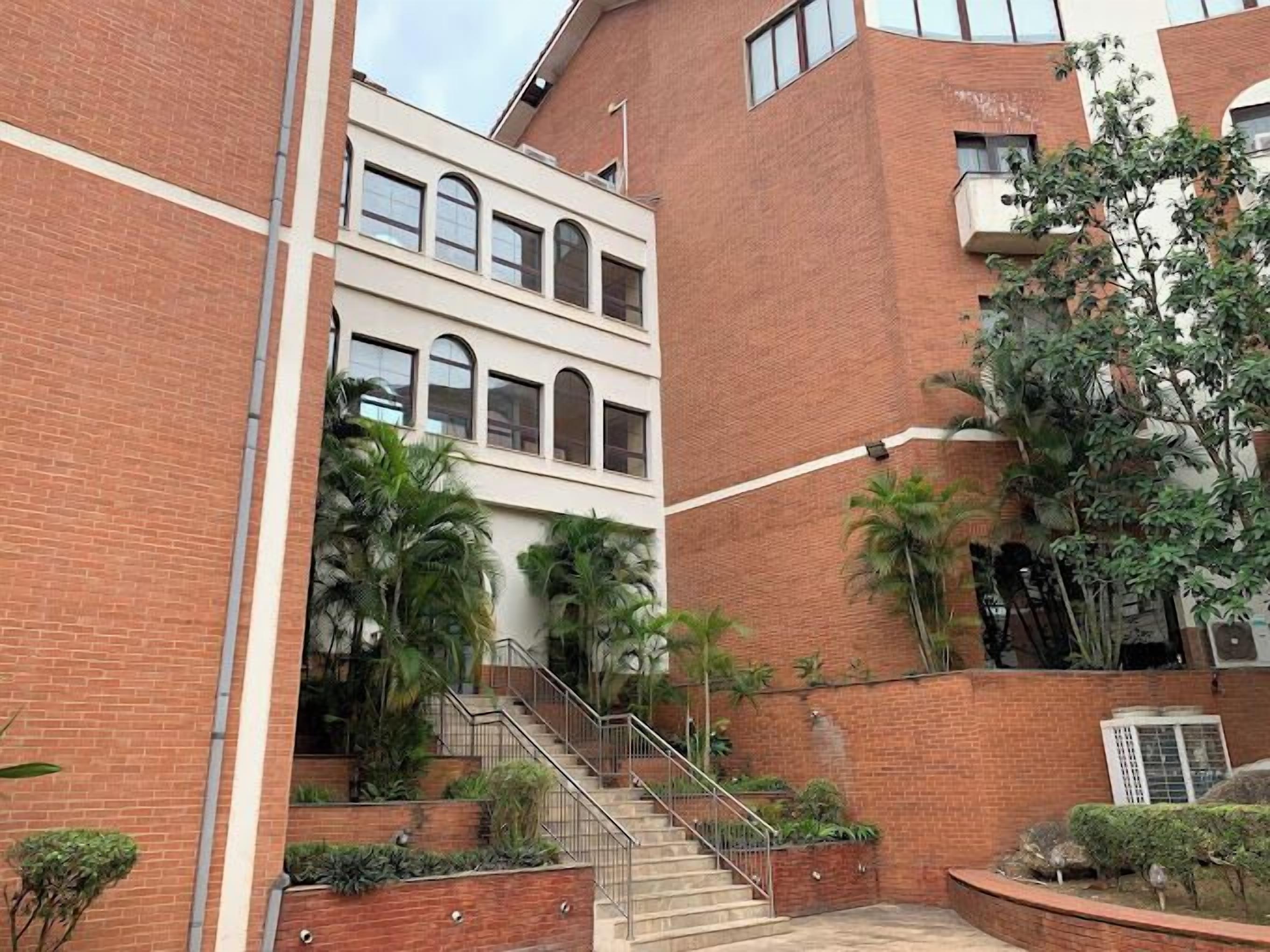 Um edifício de vários andares com uma escadaria que leva a um nível superior, cercado por muros de tijolos e palmeiras.