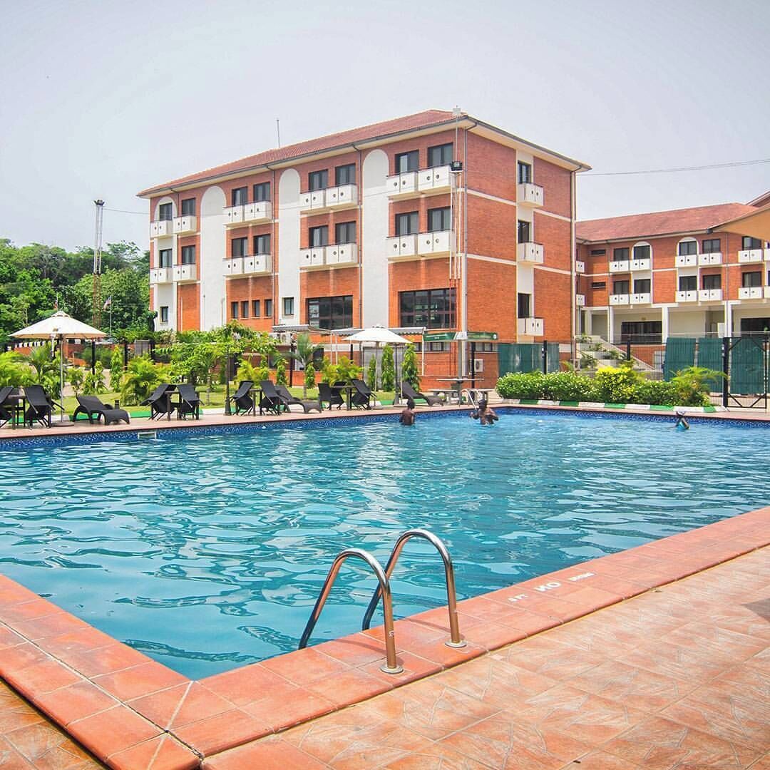 A swimming pool with lounge chairs and a building with multiple balconies in the background.