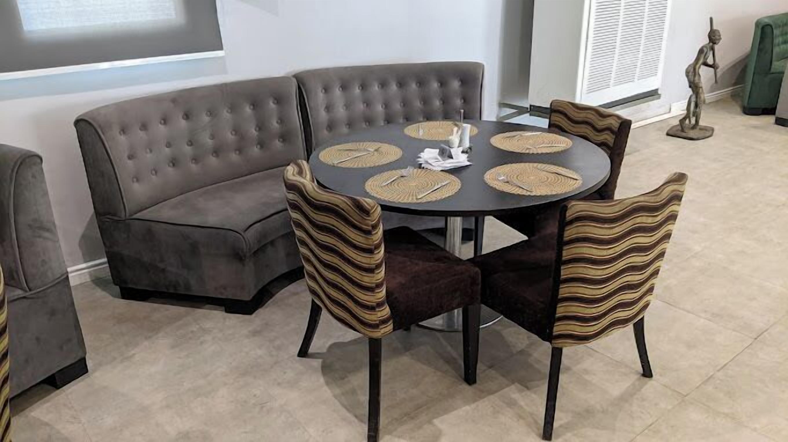 A dining area with a round table, four chairs, and a grey upholstered sofa.