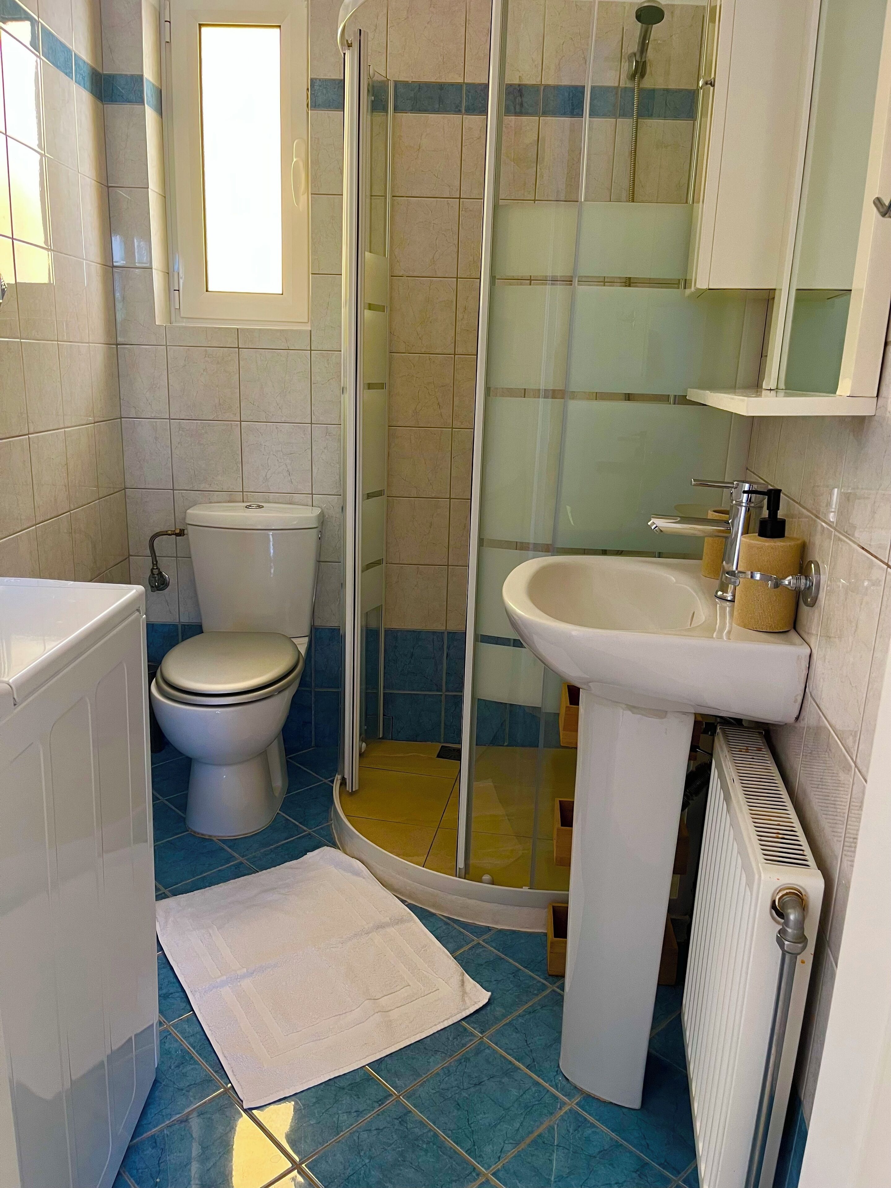 A bathroom with a toilet, a shower enclosure, a sink, and a radiator.