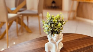 Zona pranzo con tavolo in legno, sedie e un vaso decorativo bianco con verde.