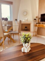 Un comedor con una mesa de madera, sillas y un jarrón blanco decorativo con follaje verde.