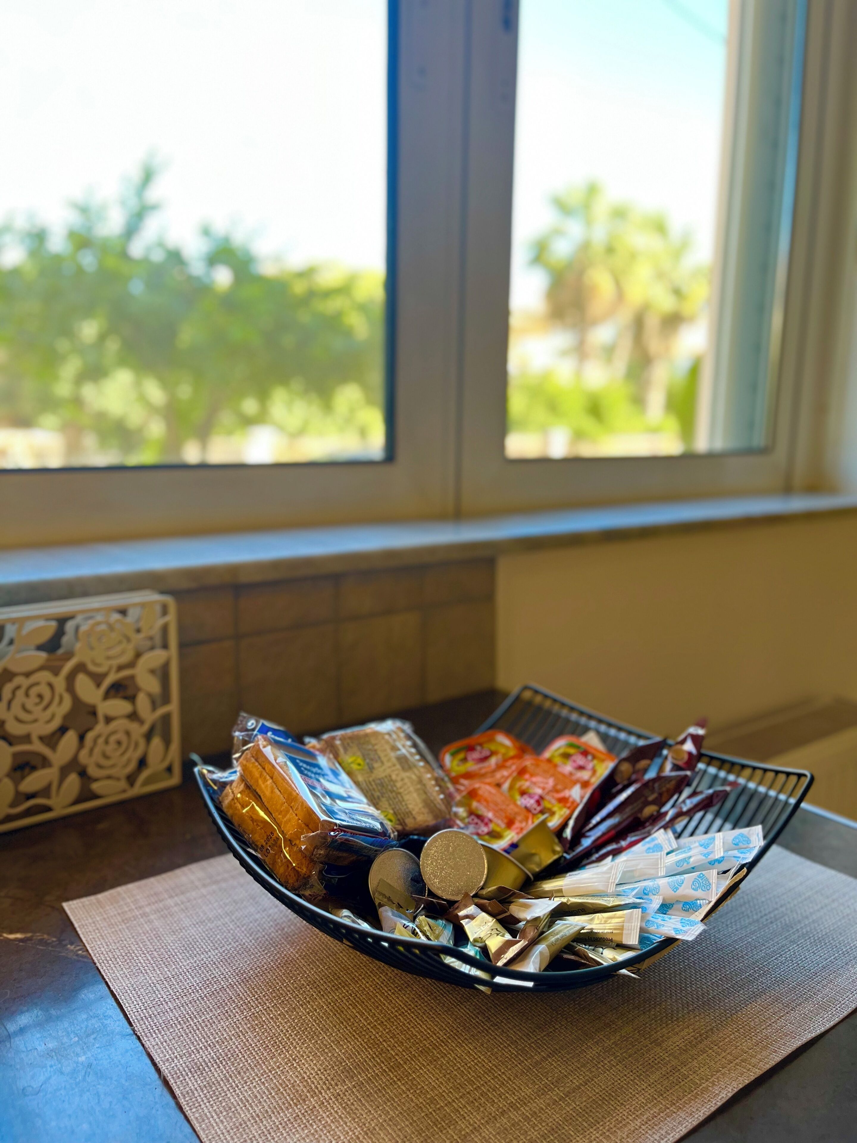 Una cesta con diversos productos alimenticios envasados sobre una encimera de cocina cerca de una ventana.