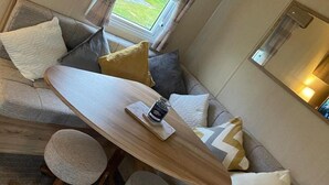 A cozy living area with a wooden coffee table, a sofa with cushions, and a small round table with a candle. - Seaside Caravan Retreat in Craig Tara (Ayr)