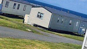 A row of mobile homes with a grassy area in front. - Seaside Caravan Retreat in Craig Tara (Ayr)
