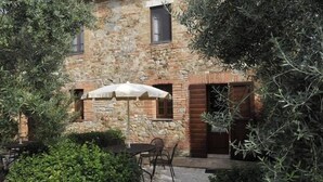Ein Steinhaus mit rustikalem Aussehen, eine Terrasse mit Tisch und Stühlen sowie ein weißer Sonnenschirm.
