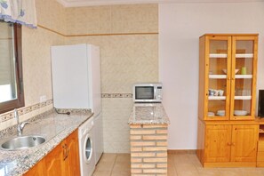 A compact kitchen with a washing machine, a microwave, and a wooden cabinet with glass doors.