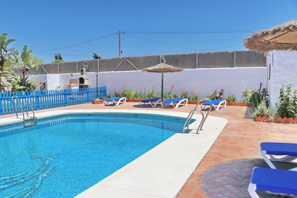 A swimming pool with blue water, surrounded by a white wall, a blue fence, and several lounge chairs.