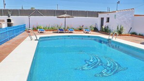 A swimming pool with a dolphin mosaic, surrounded by lounge chairs and potted plants.