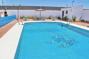 A swimming pool with a dolphin mosaic, surrounded by lounge chairs and potted plants.