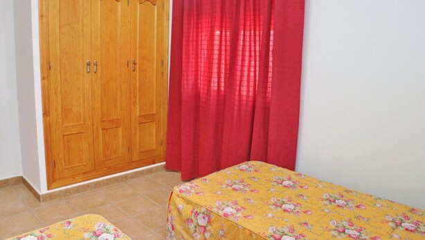 A bedroom with a wooden wardrobe, a red curtain, and a bed with a floral bedspread.