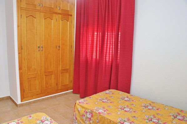 A bedroom with a wooden wardrobe, a red curtain, and a bed with a floral bedspread.