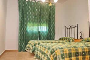 A bedroom with two beds, green curtains with a floral pattern, a metal headboard, and a bedside lamp.