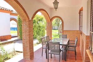 An outdoor patio with a table and chairs, brick arches, and a view of a garden.