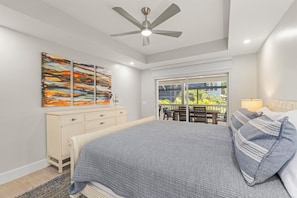 A bedroom with a bed, a ceiling fan, a dresser, a window with a view, and abstract art on the wall. - Beach, Please! | East Rocks Oasis with Pool and Short Walk to the Beach! (Sanibel)