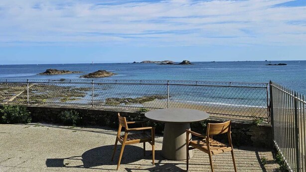 A seaside patio with a round table and two chairs, overlooking the ocean and rocky outcrops. - Magnifique vue Pleine mer à la Perle Marine - La Terrasse (Dinard)
