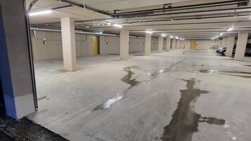 A multi-level underground parking garage with concrete floors and pillars, equipped with overhead lighting and drainage grates.