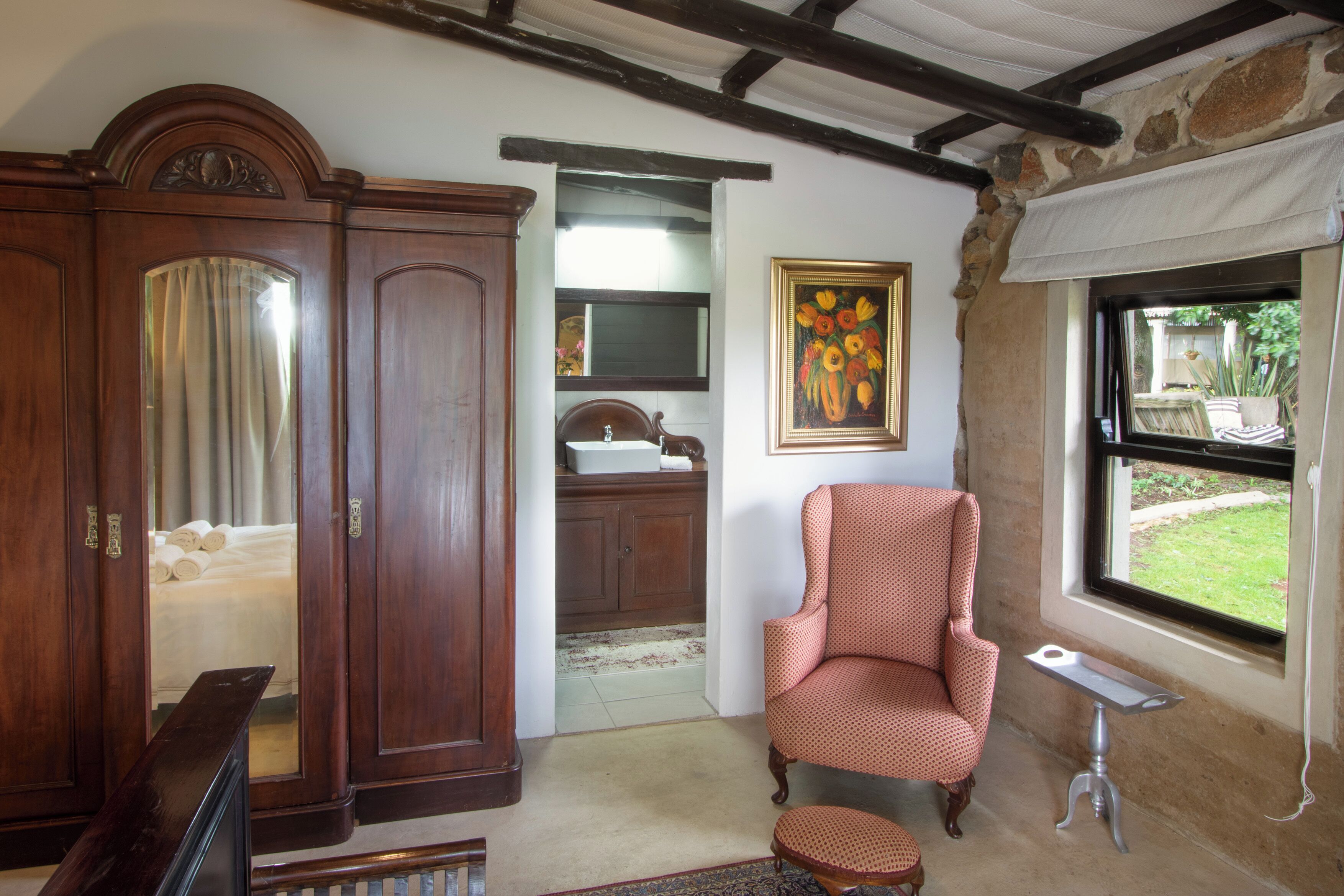 A room with a wooden wardrobe, a red armchair, a small table, and a window with a view of greenery.
