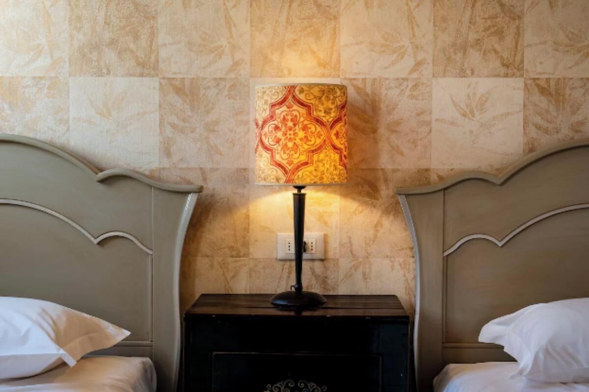 A hotel room with two beds, a nightstand with a lamp, and a wall with patterned tiles.