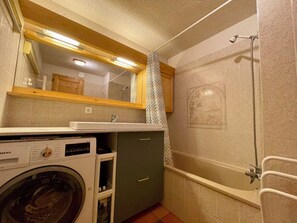 Bathroom features a bathtub, sink, and washing machine, with a towel rack and mirror.