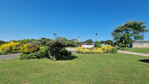 A grassy area with a building, a tree, and a clear blue sky. - D&ashortbreaks-stmargaretsbay-parking (Dover)