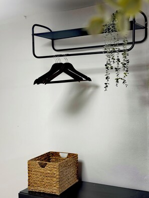 A wall-mounted rack with two black hangers and a hanging plant. Below, a woven basket is placed on a black surface. - Athens Heartbeat Stay Lykavittos View & Acropolis Glimpse (Athens)