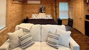 Un dormitorio rústico de cabaña con una cama grande, un sofá con cojines estampados y un techo de madera con iluminación empotrada.