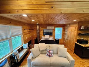 L’intérieur chaleureux d’un chalet avec un canapé, une cheminée, un lit et un coin cuisine.