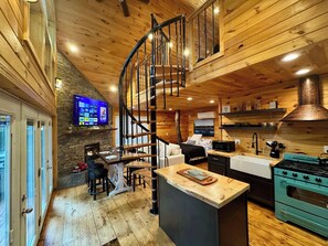 A modern kitchen with a central island, a built-in stove, and a spiral staircase. - Treehouse Duo Lakefront  2 Private Hot Tubs (Belgrade)