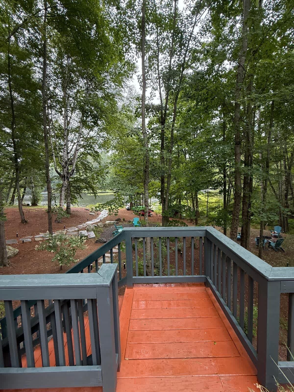 A wooden deck with a railing, surrounded by trees and a view of a park area.