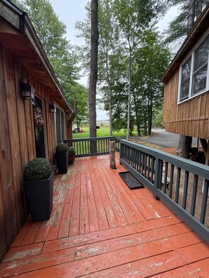 A wooden deck with a railing, potted plants, and a view of a forested area. - Treehouse Duo Lakefront  2 Private Hot Tubs (Belgrade)