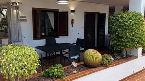 Un espace extérieur abrité, aménagé avec une table et des chaises, et entouré de différentes plantes et d’un cactus.