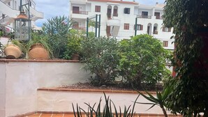 Une cour dallée de carreaux de terre cuite, agrémentée de plantes en pot et offrant une vue sur des bâtiments blancs dotés de balcons.