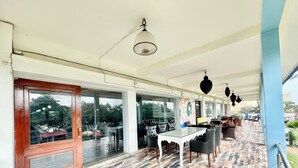 A covered outdoor seating area with tables and chairs, large windows, and a patterned floor. - Hotel V-i sea view - Puri  (Puri)