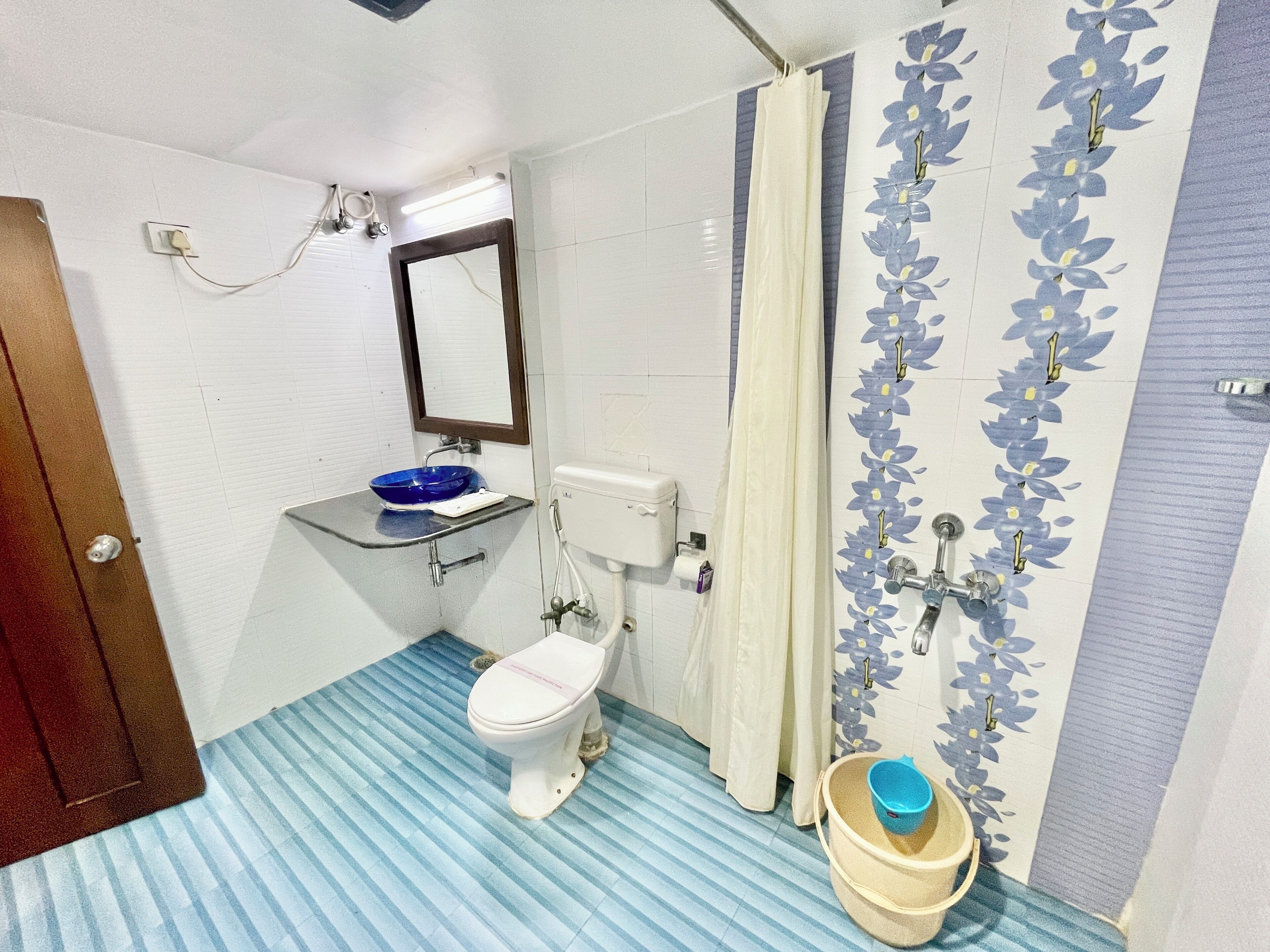 A bathroom with a toilet, sink, shower curtain, and a bucket.