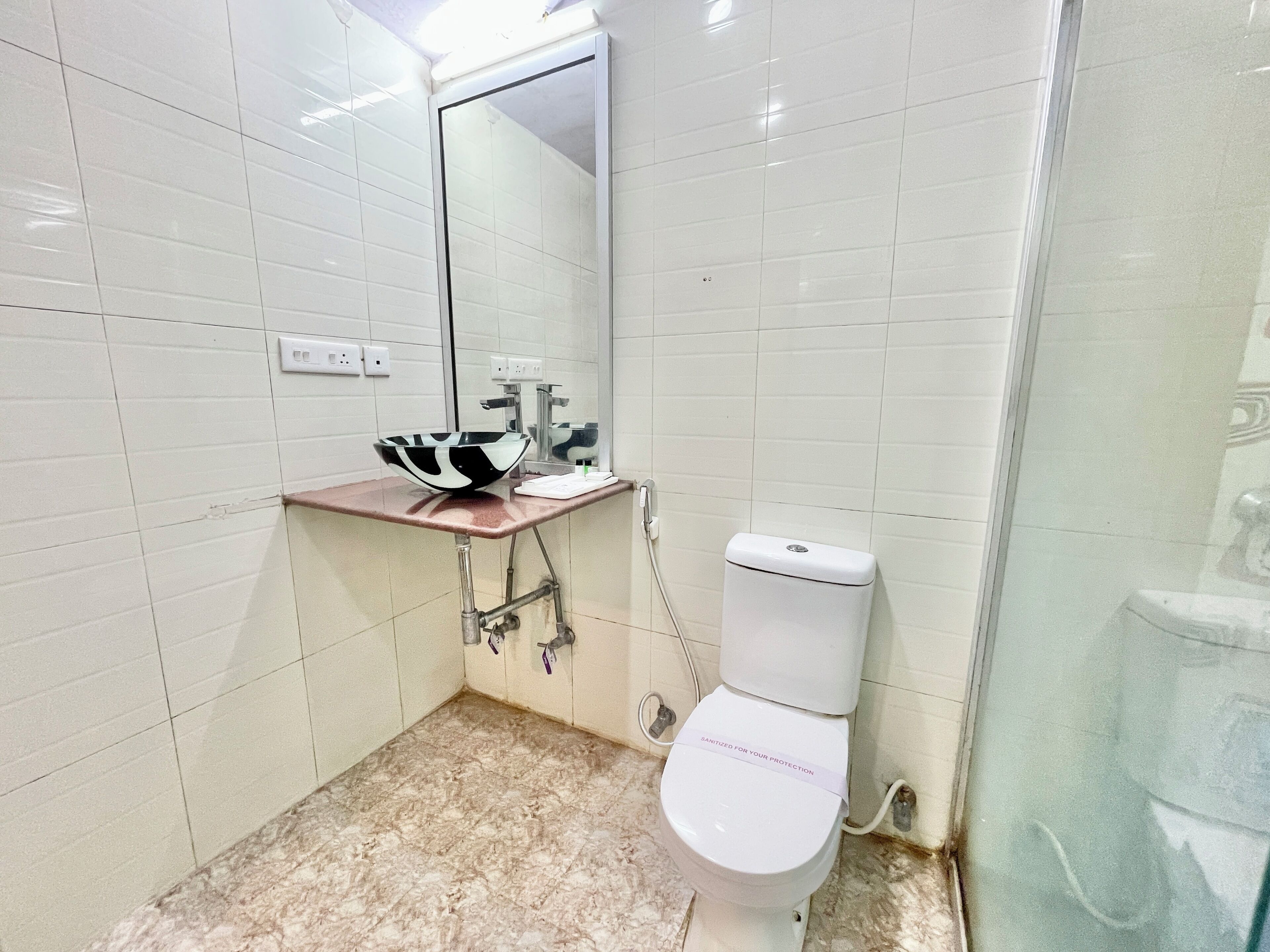 Un baño con un inodoro blanco, un lavabo con una pileta blanco y negro, y un espejo sobre el lavabo.