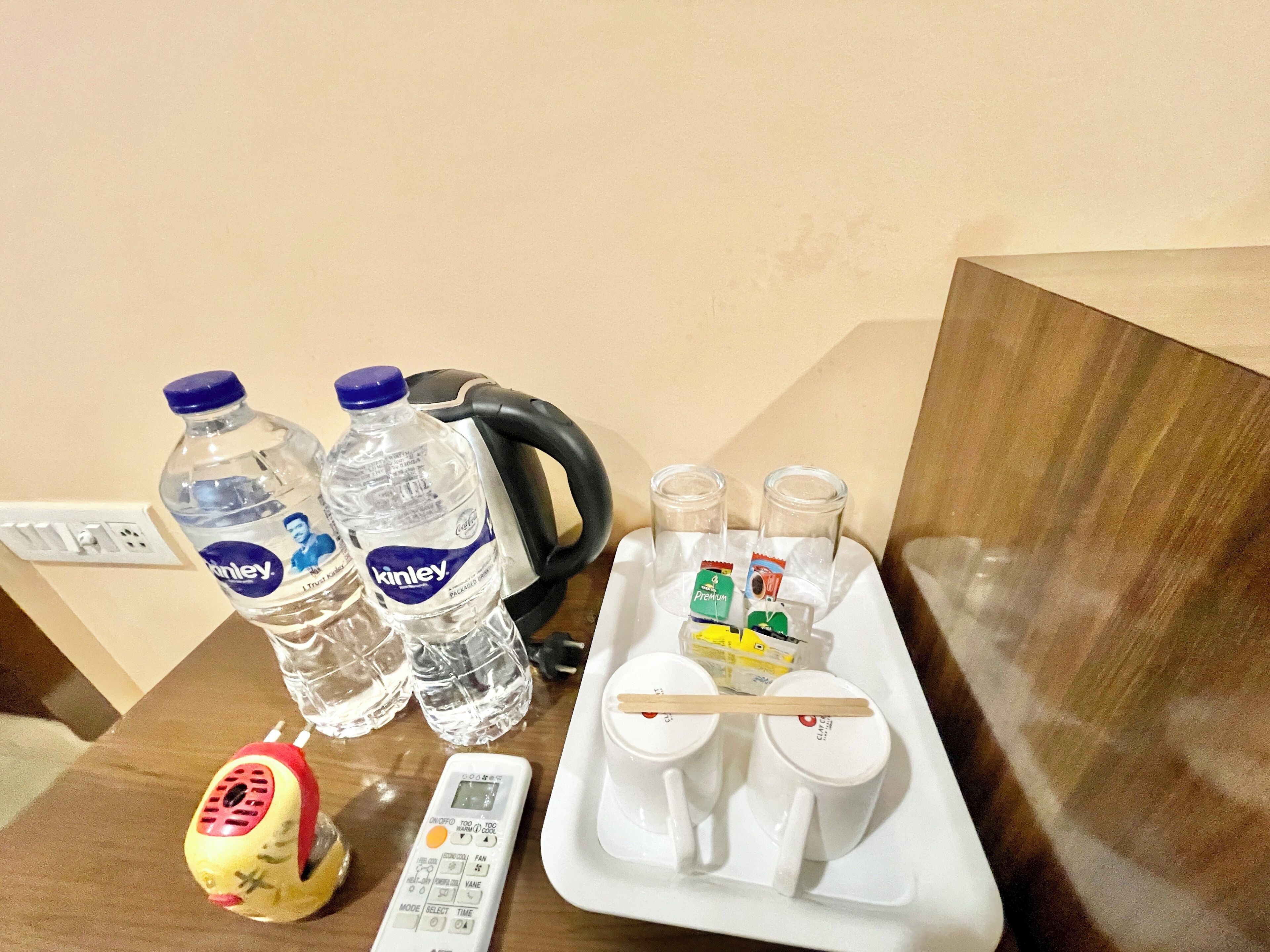 A table with two bottles of water, a kettle, a remote control, and a tray with cups and condiments.