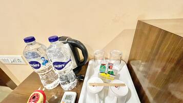 A table with two bottles of water, a kettle, a remote control, and a tray with cups and condiments.
