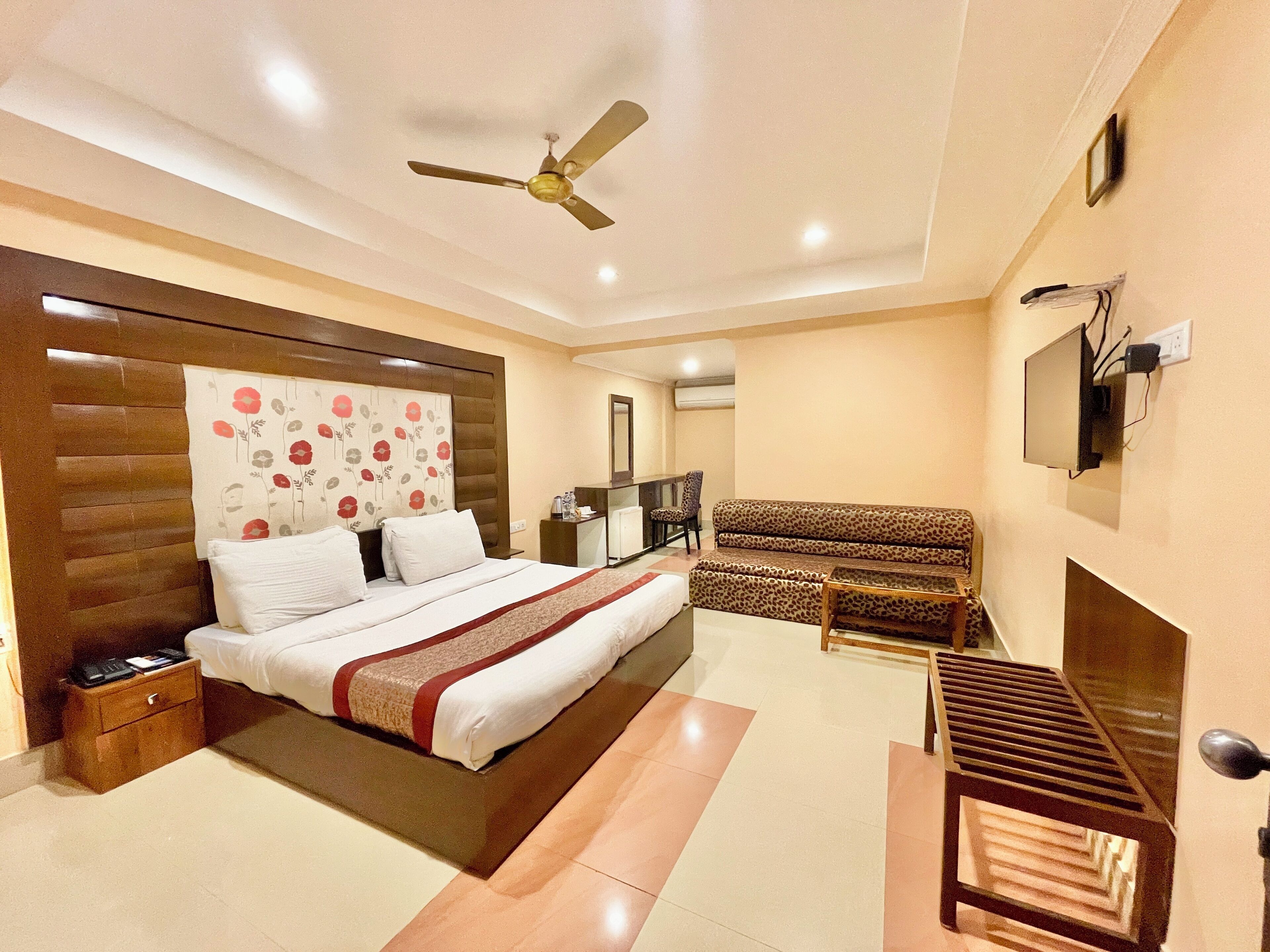 Una habitación de hotel con cama, sofá, televisión y ventilador de techo.