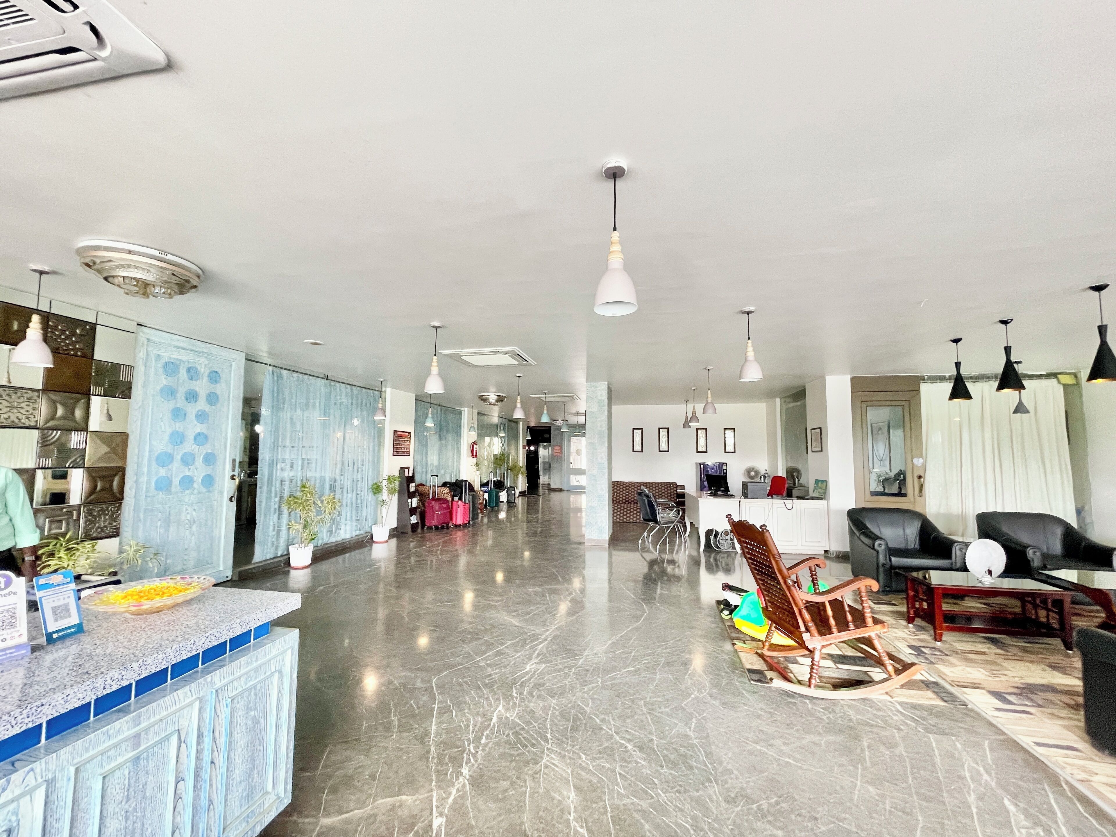 A spacious hotel lobby with a marble floor, a reception desk, several seating areas, and modern pendant lighting.