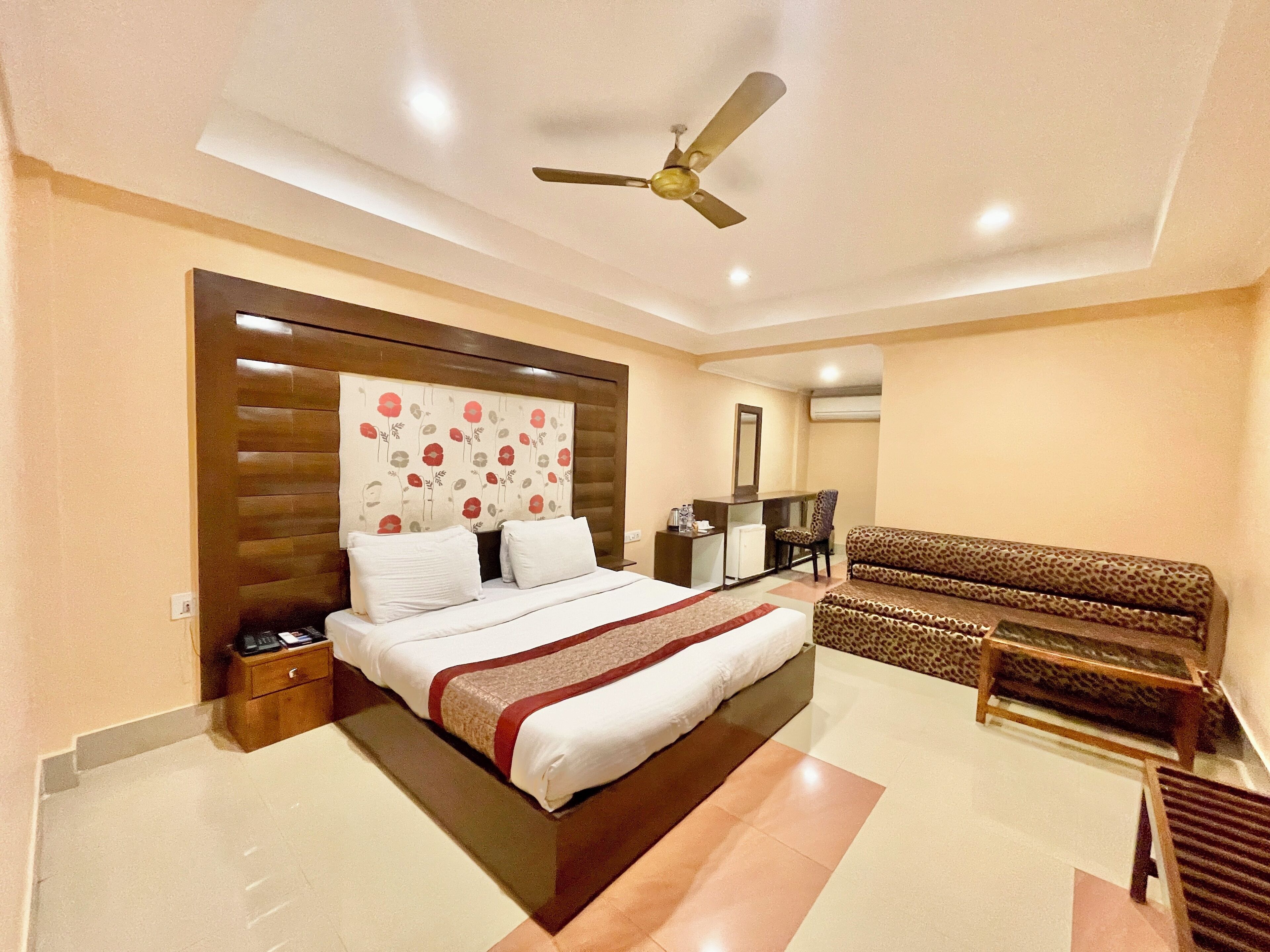 A modern hotel room with a large bed, a sofa, a desk, and a ceiling fan.