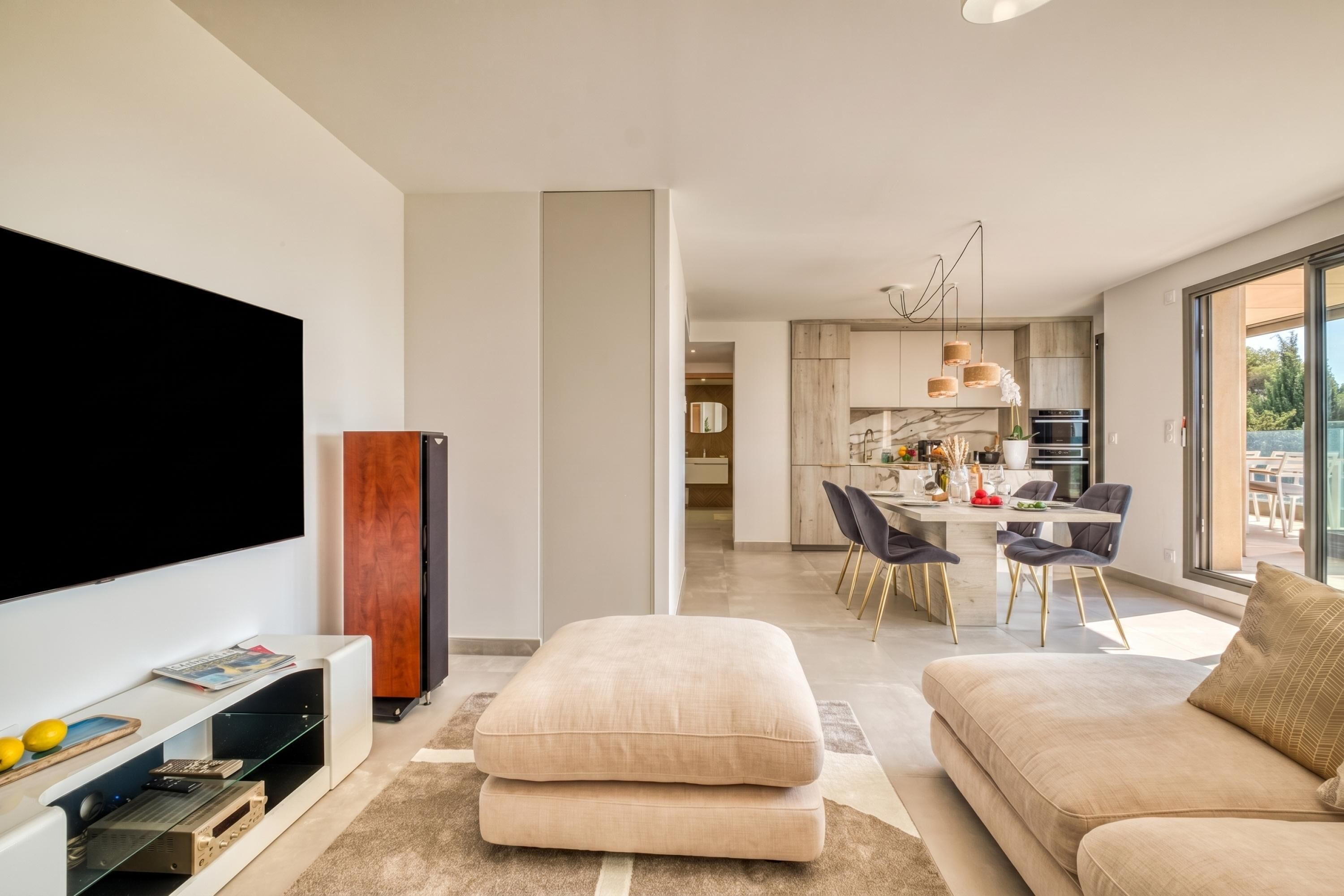 A modern living room with a flat-screen TV, ottomans, a sofa, and a dining area with chairs and a table.