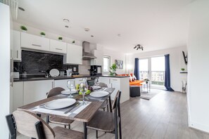 A modern kitchen with white cabinets, a black marble backsplash, and a dining area with a wooden table and chairs. - Top-rated Penthouse - King Size Bed & Free Parking (Romford)
