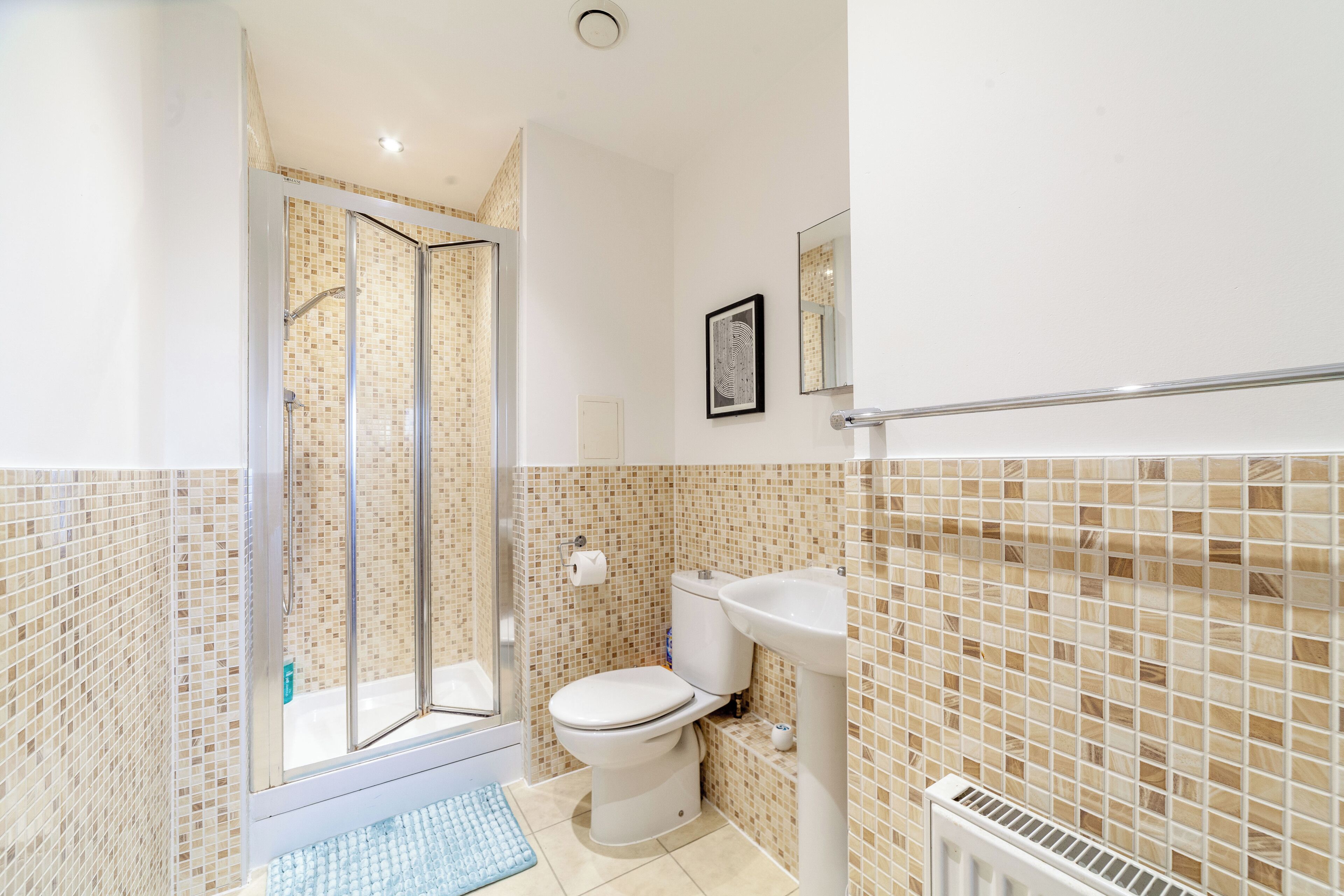 Une salle de bain équipée d’une douche, de toilettes, d’un lavabo et d’un tableau encadré au mur.