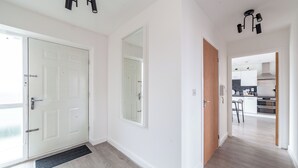 A hallway with a white door, a mirror, and a kitchen area visible through an open door. - Top-rated Penthouse - King Size Bed & Free Parking (Romford)