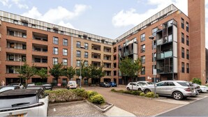 A multi-story residential building with a brick facade, multiple balconies, and a parking area with several cars. - Top-rated Penthouse - King Size Bed & Free Parking (Romford)