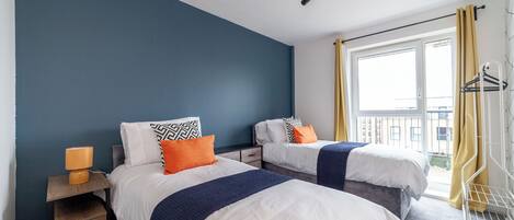 Une chambre avec deux lits, une table de chevet, une lampe et une fenêtre avec des rideaux.