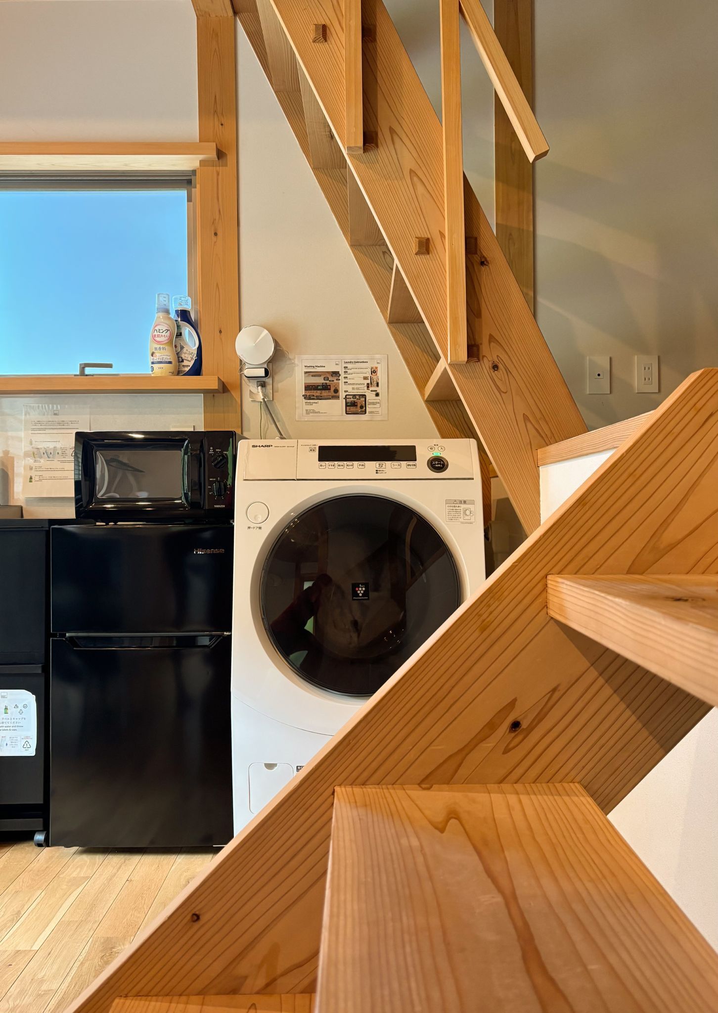 Eine Küche mit Mikrowelle, Kühlschrank und Waschmaschine. Eine Holztreppe führt zu einer weiteren Ebene.