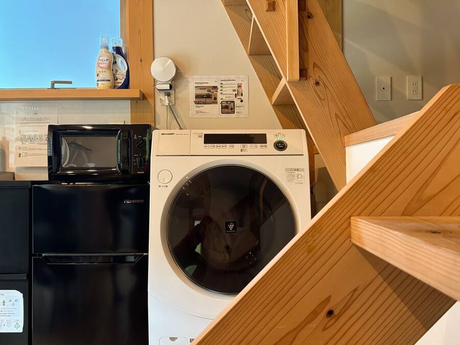 Eine Küche mit Mikrowelle, Kühlschrank und Waschmaschine. Eine Holztreppe führt zu einer weiteren Ebene.